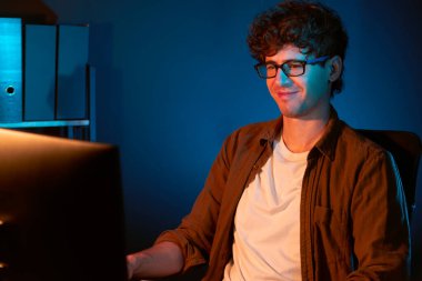 Genç işadamı, Neon Light Modern Ofis 'teki yeni proje surround çalışma masası için kağıt üzerinde tasarım düşünüyor. E-posta ile hediye göndermeden önce not defterine yeni bir iş düşünüyorum. Toplayıcı.