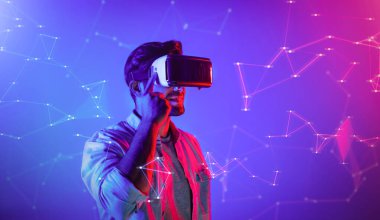 Zeki beyaz adam neon ışıkta dururken VR gözlük takıyor. Teknoloji yeniliklerini kullanarak görsel gerçeklik gözlüğünü kullanarak metaevren ya da görsel dünya programını bağlayabiliyor. Sapma.