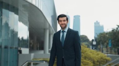 Profesyonel iş adamı hareket ediyor ve kameraya bakarken ayakta duruyor. Gülümseyen yönetici kameraya kendinden emin bir şekilde gülümsüyor. Mimari binada takım elbiseli yatırımcıların yakın çekimi. Sevinçli..
