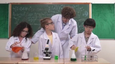 Kafkasyalı zeki öğretmen, meraklı öğrencilerin laboratuardaki deney kabına renkli sıvı dökmesini destekler. Yaratıcı çocuklar deney yapmaya ve biyokimyasal örnekleri incelemeye konsantre olurlar. Pedagoji.