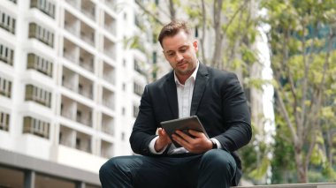 Kafkas iş adamları yeşil şehirde otururken tablet üzerinde çalışıyorlar. Uzman yönetici iş ekibiyle çalışırken finansal veri analizi yapmak ve aramak için tablet kullanıyor. Urbane.