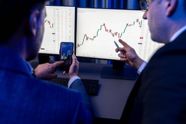 İki borsa simsarı akıllı telefon ve dinamik dijital para birimi dizüstü bilgisayar sunucusu verilerini araştırıyor. Yatırımcılar, işyerinin dekoratif neon mavi ışığındaki pazar hisselerini analiz ediyorlar. Satılabilir.