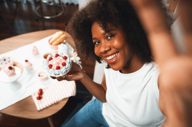 Genç ve güzel Afrikalı blogcu akıllı telefondaki selfie ile konsept özel mutfak konseptinde kek sunuyor. Favori tatlı fırın yemeğiyle sosyal medyanın yaratılması. Tatlandırıcı.