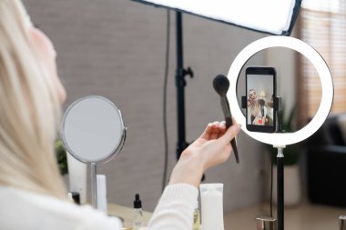 Sosyal medya için güzellik ve kozmetik video içeriği hazırlayan genç bir kadın. Güzellik blogcusu seyirciye güzellik hizmetini nasıl uygulayacağını ya da kamera karşısında takipçiyi nasıl izleyeceğini gösteriyor. Blithe