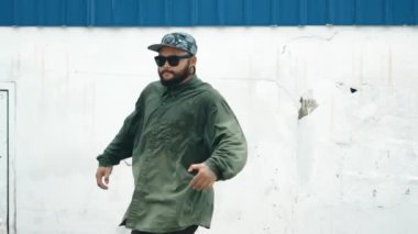 Sokak ortasında mavi duvarlı hippi dansçı ayak basamağı. Asyalı break dansçı kollarını açarken sokak dansı yapıyor. Hip hop koreografı enerjik bir dans sergiliyor. Açık hava sporu 2024 hiphop..