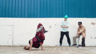 Genç Asyalı dansçı hip hop tarzında dans ediyor ve çok kültürlü arkadaşları duvarın arkasında tezahürat yapıyor. Çekici yakışıklı adam mavi arka planda kollarını uzatıyor. Açık hava sporu 2024 hiphop..