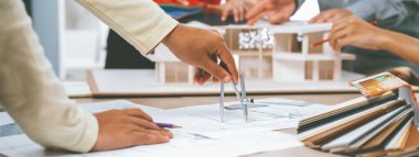 Profesyonel mimar takımı sürdürülebilir ev malzemelerini seçerken, yetenekli mühendis de ev modeli ve renk paletini kullanarak toplantı masasına yerleştirir. - Yakın çekim. Değiştirilmiş.