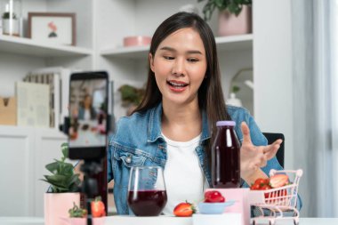 Gülümseyen, güzel Asyalı genç, lezzetli karışık çilek ve kiraz suyu detoksu içeceklerini inceleyen, sosyal medyada özel promosyon satışı için sağlıklı ürünler sergileyen. Taktik.