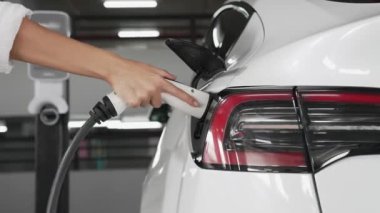Genç bir kadın, EV elektrikli arabasıyla şehir merkezindeki alışveriş merkezinin otoparkına gidiyor. Sürdürülebilirlik yaşam tarzını yeşil, temiz, yeniden şarj edilebilir elektrikli araç iç organlarıyla şarj ediyor.
