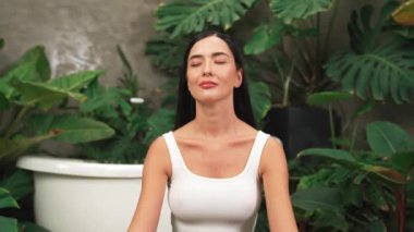 Sabah yoga ve meditasyon yapan genç bir kadın bitki yaprağıyla doğal bahçede yalnızlığın tadını çıkarıyor ve meditasyon yapıyor. Farkındalık aktivitesi ve sağlıklı zihin yaşam tarzı. Blithe