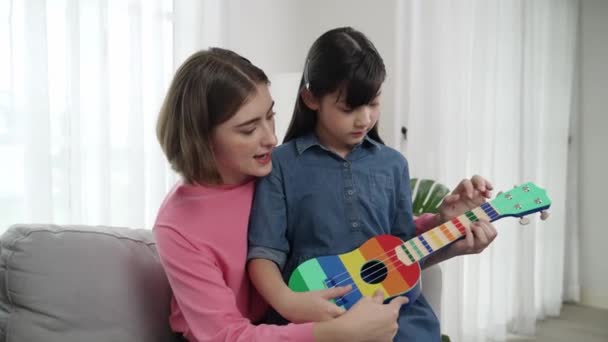 Szczęśliwa Dziewczyna Gra Ukulele Podczas Gdy Kaukaska Mama Uczy Wyjaśnić — Wideo stockowe