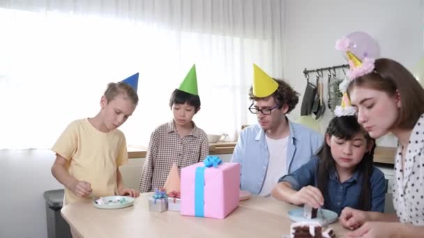 ハッピーファミリーは 現代のキッチンでパーティーハットを着用しながら娘の誕生日ケーキを食べています 風船で飾られたキッチンで友人と誕生日を祝いながらケーキを食べるエネルギッシュかわいい子供 ペダゴロジー — ストック動画