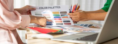 Profesyonel iç mimarın kırpılmış bir görüntüsü, renk örnekleri ve renk paleti belgeleriyle karşılaştırarak iş arkadaşlarıyla renk materyalini tartışıyor. Yaratıcı tasarım konsepti. Değiştirilmiş.