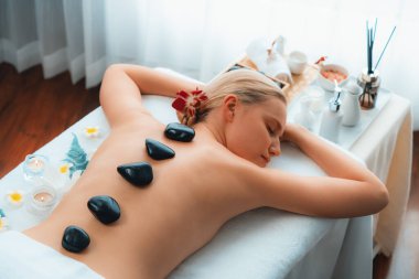 Lüks tatil köyündeki kaplıcalarda sıcak taş masajı. Gün ışığı sükunet ortamında, mutlu kadın müşteri bazalt taş masajından zevk alıyor. Rahatlatıcı bir sıcaklıkla vücudun üzerinde süzülüyor. Sessiz.