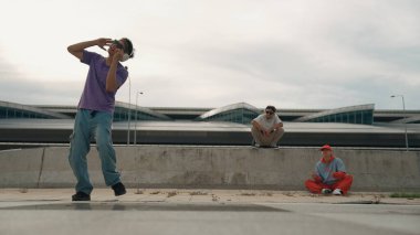 Bir grup yetenekli break dansçı, ona bakan ve tezahürat yapan arkadaşlarıyla sokak dansı yapıyor. Yakışıklı hippi çocuk sokakta müzik dinlerken dans ediyor. Açık hava sporu 2024. Yumuşak bir şekilde..