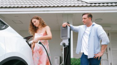 EV şarj istasyonundan çevreci bilinci açık elektrikli araca sahip mutlu ve sevimli bir çift. EV araba teknolojisi gelecekteki sürdürülebilirlik için alternatif ulaşım aracı olarak kullanılıyor. Eşzamanlama