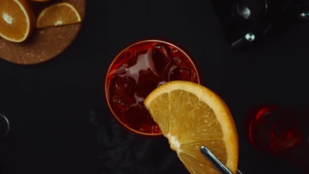 宏观地理学 从自上而下的角度来体验混合尼葛洛尼鸡尾酒的艺术 配上鲜活的橙片 所有这些都与戏剧性的黑色背景相映成趣 酒精中毒可赔偿性 — 图库视频影像