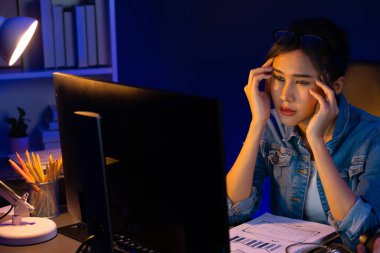 Stresli, genç, güzel Asyalı yaratıcı proje yaratıcısı sosyal medyayı araştırmak için bilgisayara bakıyor ve geceleri daha çok neon modern ofisin planlama kanalı stratejisine ulaşılıyor. Taktik.