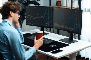 İki ekranda piyasa grafiği verilerine odaklanan ve elinde modern ofiste arka manzaralı kahve fincanı tutan genç bir tüccar. Dinamik para bozdurma oranını analiz etme kavramı. Toplayıcı.