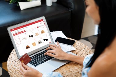 Genç bir kadın dizüstü bilgisayarla ürün sipariş eder ya da satın alır ve akıllı telefondan işlem ödemesi yapar. İnternet bankacılığı vasıtasıyla internet üzerinden kredi kartıyla online alışveriş hayatı. Blithe