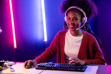 Neon renkli aydınlatma odasında kulaklık takan Afrika kökenli Amerikalı kız flamalı Esport yetenekli takımıyla online dövüş yapıyor. Rakiplerini kazanmak için strateji planlayan diğer oyuncularla konuşmak. Tatlandırıcı.