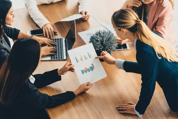 Modern işyeri ofisindeki diğer iş kadınlarıyla grup toplantısındaki iş kadını masada dizüstü bilgisayar ve belgelerle konuşuyor. Kurumsal iş dünyası konsepti. uds