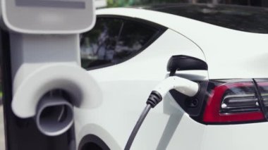 Yavaş çekim EV elektrikli araba yazın yeşil sürdürülebilir şehir parkı bahçesinde şarj oluyor. Elektrikli araç iç organları için kentsel yaşam tarzında sürdürülebilir temiz şarj edilebilir enerji