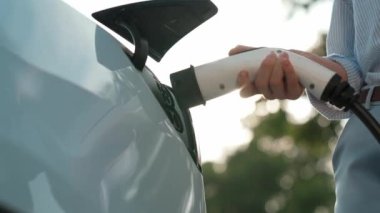 Yolculuk sırasında doğal ormanlarda ya da sonbahar sezonu gündoğumu aydınlatmalı ulusal parktaki elektrikli araba için şarj olan genç bir kadın. Arkadaşça bir seyahat tatili ve tatil. Yükselt