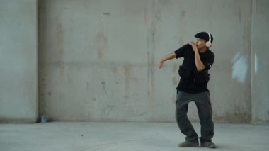 Kulaklıktan çimento arka planda müzik dinlerken break dans pratiği yapan yakışıklı bir hippi. Sokak dansçısının hareketli çekimi robot dansı yapar. Açık hava sporu 2024. Modern dans. hiphop.