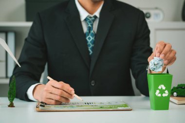 İşadamı, daha yeşil bir çevre ve sıfır kirlilik için geri dönüşüm yaparak şirketlerin çevre dostu atık yönetimi üzerindeki çabalarını sembolize eden küçük geri dönüşüm kutusuna kağıt atığı koydu. Döngü