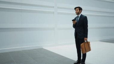Yetenekli yönetici, iş arkadaşıyla proje hakkında konuşmak için telefon görüşmesi yapıyor. Yakışıklı erkek lider, beyaz arka planda yürürken haber vermek ve cep telefonunu cebe indirmek için iş ekibini arıyor. Sevinçli..