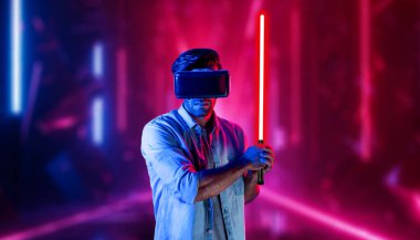 Lazer kılıcı tutan ve VR gözlük takan oyuncu. Beyaz adam, neon şatonun etrafında dikilirken görsel gerçeklik kulaklığı kullanıyor. Yenilik teknolojisi. Sapma.