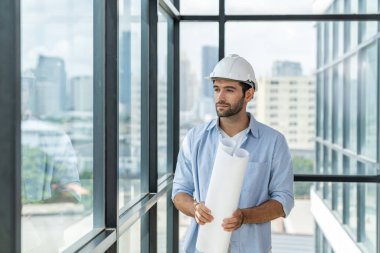 Proje planı yaparken gökdelen ve şehir manzarasına bakan günlük kıyafetli profesyonel mimar ya da erkek işçi. Yaratıcı tasarım, inşaat mühendisliği, bina inşaatı. İzleme.