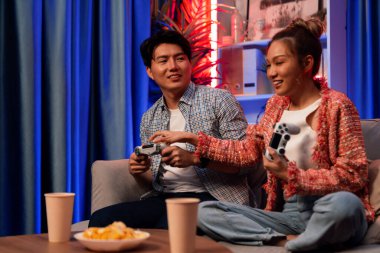 Neşeli, gülümseyen bir çiftin koltuğunda oturup oyun oynuyorlar. Oyun konsolu, hazır aperatifler ve içecekler, modern neon ışıklı, rahat oturma odasında eğlenceli bir rekabet seviyesinde. İnfobahn.