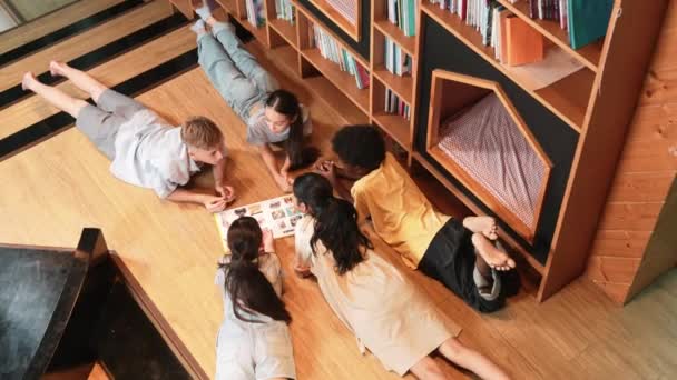 一群各种各样的孩子在图书馆看书时 成圈地躺着 女孩一边指点感兴趣的话题 一边和可爱的朋友聊天 一边分享杂志的头像 — 图库视频影像
