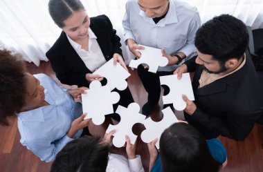 Çeşitli şirket çalışanları, ortaklık ve takım çalışmasını temsil etmek için bulmaca parçalarını birleştirerek ofiste işbirliği yapıyor. Yapboz 'u birleştirerek iş dünyasındaki birlik ve sinerji. Uyum