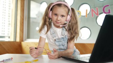 Çalışırken kulaklık takan ve kameraya bakan bir kız. Beyaz çocuk dizüstü bilgisayar, tornavida ve kablolarla bilim deneyi yapıyor. Akıllı online sınıf. Etkinlik.