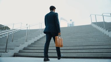 Akıllı bir iş adamının elinde çantayla merdivenlerden yukarı çıkışının en üst görüntüsü. Profesyonel proje yöneticisi merdivenlerden çıkıp işyerine gidiyor. Yeteneklerini arttırmak, terfi almak, seyahat etmek. Sevinçli..