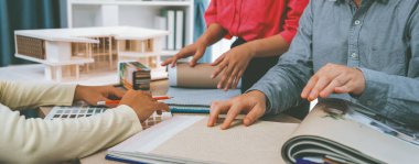 Yetenekli iç dizayn ekibi perde malzemelerini dikkatle seçerken iş arkadaşı da toplantı masasının üzerinde ev modeliyle perdenin rengini seçiyor. Yaratıcı tasarım konsepti. Değiştirilmiş.