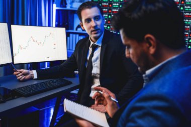 İki borsa simsarı dinamik yatırım grafiğini tartışıyor, yüksek kar eğilimli döviz borsası. İş yerindeki neon ışıkta finansal fayda verileri monitörde gösteriliyor. Satılabilir.