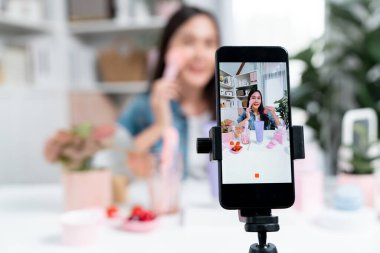 Seçici odak akıllı telefonu ile genç ve güzel Asyalı makyaj fırçası yanak testi koleksiyonunu pastel renkli, sosyal medyada tanıtım yapmak için ışıldayan bir ruh hali gösteriyor. Taktik.
