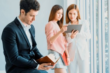 Kitap okuyan ve iş yerinde iş arkadaşları ve arkadaşlarıyla çalışan genç ve yakışıklı bir işadamı. Kurumsal iş adamları grubu. uds