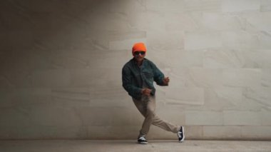 Profesyonel Asyalı hipster gri arka planda break dans yapıyor. Sokak dansçısı hip hop dansı yaparken şık bir hip hop kıyafeti giyer ve funky müzik eşliğinde dans eder. Açık hava sporu 2024. Yumuşak bir şekilde..