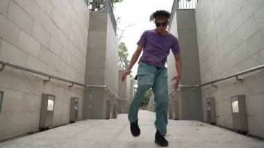 Profesyonel break dansçı dar koridorda sokak dansı yapıyor. Yetenekli mutlu Asyalı hipster, B-boy 'a dar duvarda adım gösterirken müziğe geçiyor. Modern yaşam tarzı. Açık hava sporu 2024. Yumuşak bir şekilde..