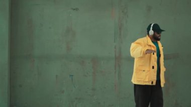 Profesyonel hipster sokak, şehir merkezinde ayak sesleri gösteriyor ya da pratik yapıyor. Genç break dansçı hareket ediyor ve kolunu ve bacağını esnetiyor. Açık hava sporu 2024. Gri arka plan. Hip hop modası. hiphop.
