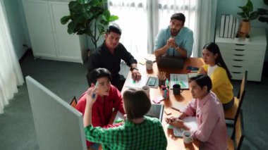 Yöneticinin ayakta ve beyaz tahtada mevcut fikirlerinin en üst görüntüsü. Bir grup insan, kadın lideri cesaretlendirmek için el çırparken sunumu dinliyor. Takım lideri plandan bahsediyor. Cemaat.