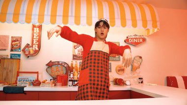 Profesyonel Asyalı restoran işçisi dans ediyor ve yemek barının arkasında duruyor. Kırmızı tişörtlü ve kırmızı önlüklü çekici garson kameraya bakarken serbest stil müziğe yöneliyor. Çılgın dans. Mutluluk.