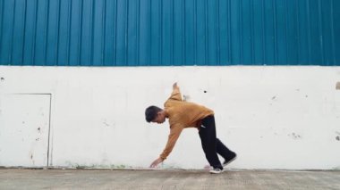 İspanyol adam kollarını açıp duvarın önünde dans ediyor. Dansçı ya da koreografın günlük kıyafetleriyle hip hop tarzında break dans yaparken ki görüntüsü. Açık hava sporu 2024 hiphop..
