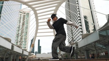 Genç Asyalı hippi şehir merkezinde insanların etrafında ayak izlerini gösteriyor. Şık bir sokak dansçısı B-boy ya da serbest dans eder. Açık hava sporu 2024. Break dans. Yumuşak bir şekilde..