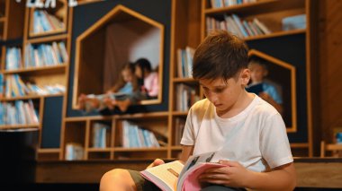 Bir grup zeki öğrenci kütüphanede otururken beyaz çocuk kitap okuyor. Çekici çocuk ders çalışıyor, çocuklar konuşurken romandan ya da kitaptan öğreniyor, eğitim hakkında sohbet ediyor. Etkinlik.